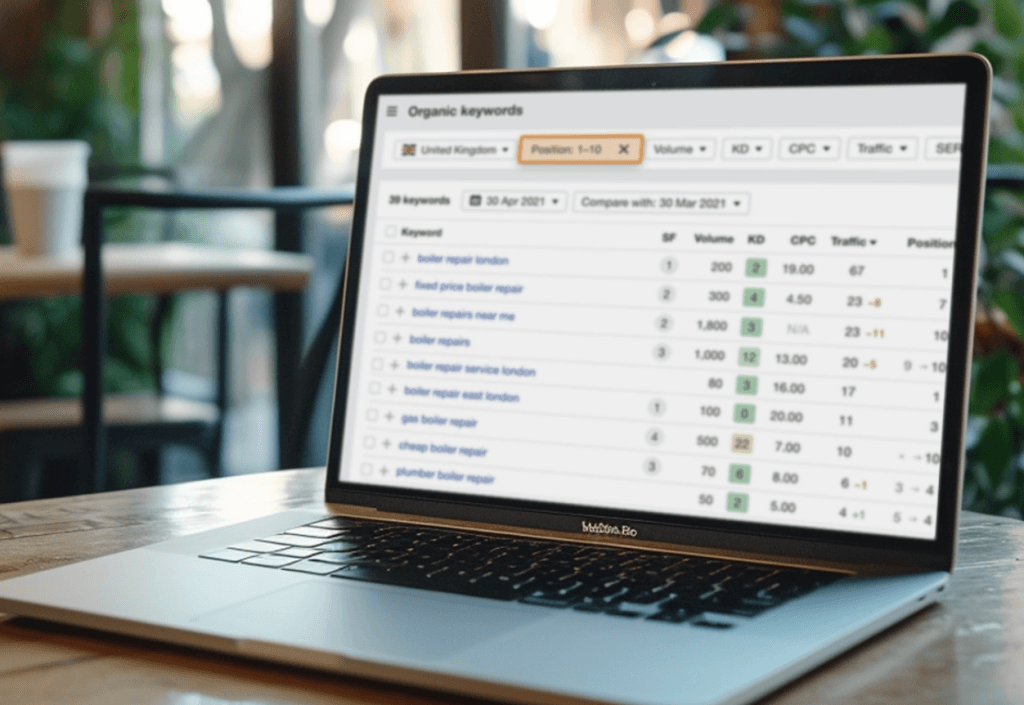 An open laptop surrounded by notebooks, pens, and a cup of coffee in a cozy home office. Laptop showing keyword ranking data on screen.