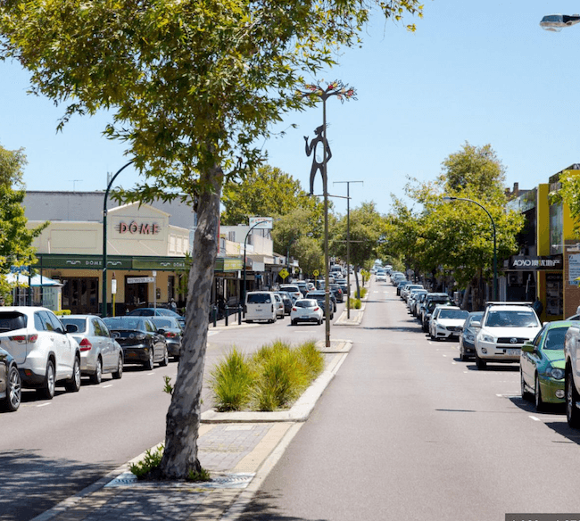Sunny street with shops, parked cars, and sculpture in Australia
